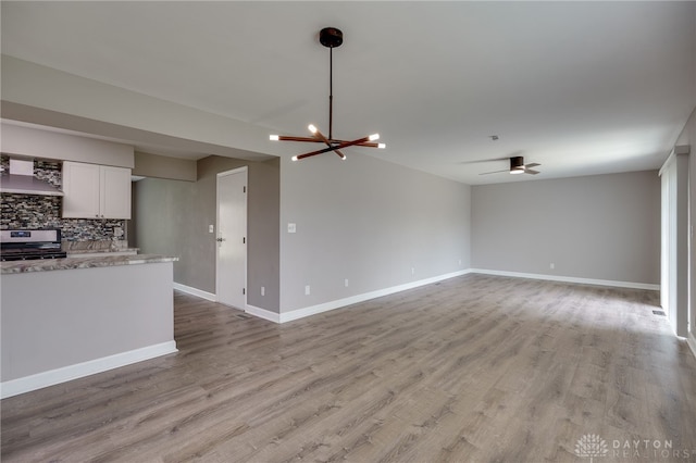 unfurnished living room with light wood-type flooring, baseboards, and ceiling fan with notable chandelier