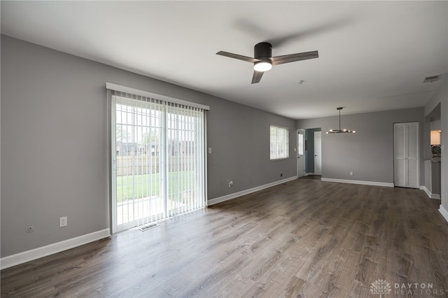 unfurnished living room with baseboards, ceiling fan with notable chandelier, dark wood-style floors, and visible vents