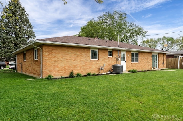rear view of property featuring a yard, brick siding, fence, and central AC unit
