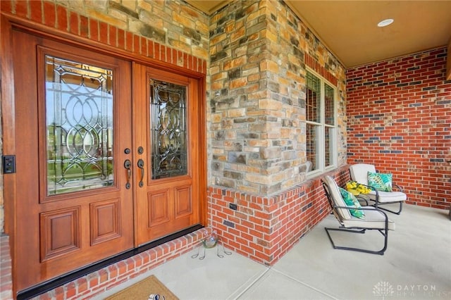 entrance to property featuring a porch, brick siding, french doors, and stone siding