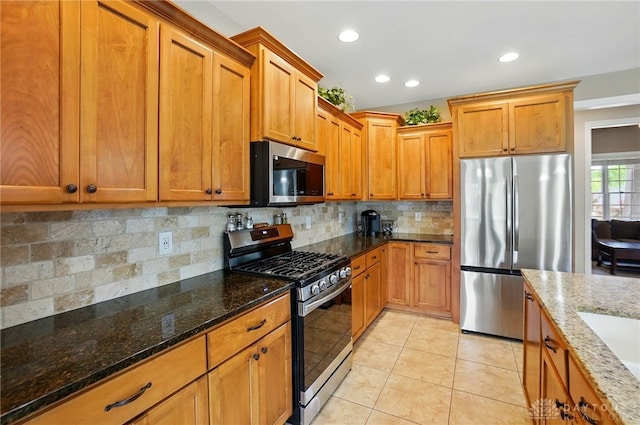 kitchen featuring appliances with stainless steel finishes, tasteful backsplash, brown cabinets, light tile patterned floors, and dark stone countertops