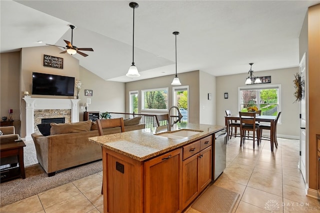 kitchen with light stone countertops, a sink, a fireplace, light tile patterned floors, and stainless steel dishwasher