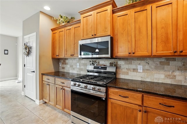 kitchen with brown cabinets, stainless steel appliances, dark stone countertops, and light tile patterned flooring
