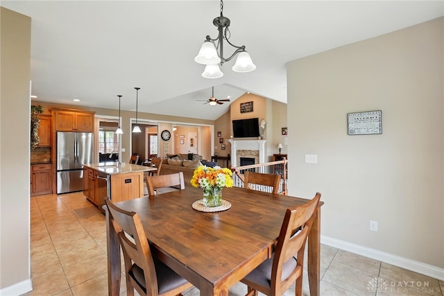 dining area with light tile patterned floors, a fireplace, ceiling fan with notable chandelier, and lofted ceiling