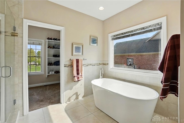 bathroom with tile patterned floors, a freestanding tub, a stall shower, and tile walls