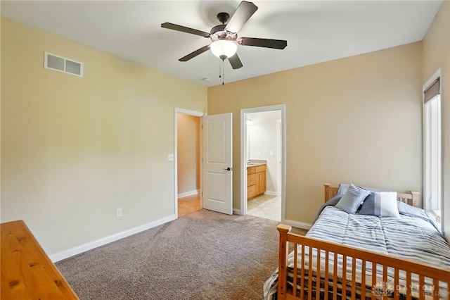 bedroom featuring ceiling fan, light colored carpet, visible vents, baseboards, and connected bathroom