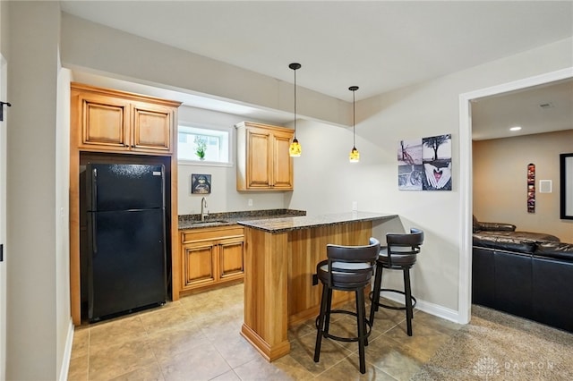 kitchen with dark stone countertops, freestanding refrigerator, a peninsula, decorative light fixtures, and a kitchen bar