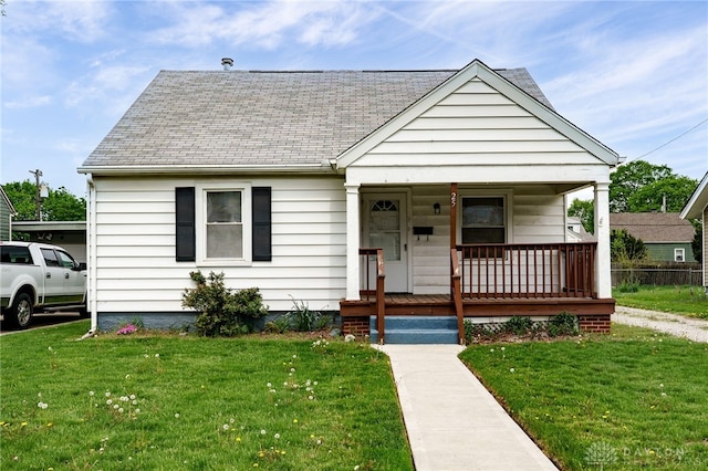 bungalow-style house with covered porch, roof with shingles, and a front lawn