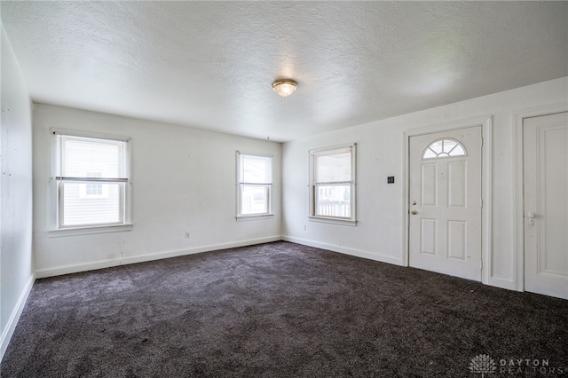 entryway with a textured ceiling, baseboards, and dark carpet