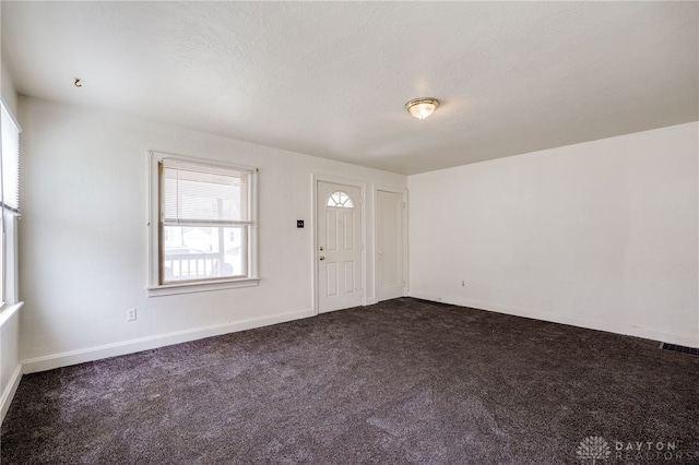 foyer entrance featuring baseboards, visible vents, and dark carpet