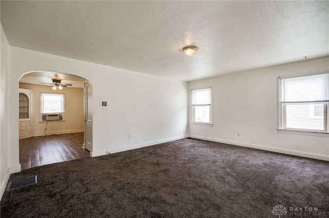 unfurnished room featuring arched walkways, baseboards, dark carpet, and visible vents