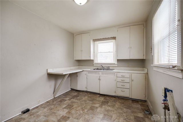 kitchen featuring baseboards, a sink, white cabinetry, and light countertops