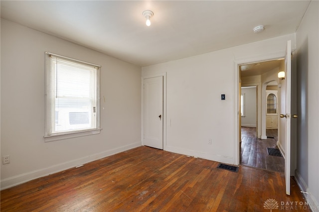 unfurnished bedroom featuring arched walkways, baseboards, dark wood finished floors, and visible vents