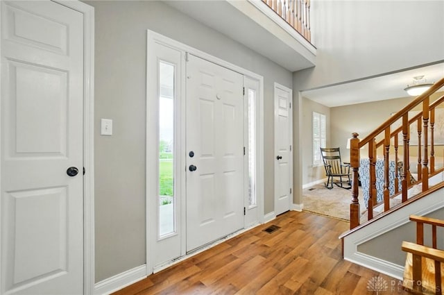 foyer entrance featuring baseboards, wood finished floors, visible vents, and stairway