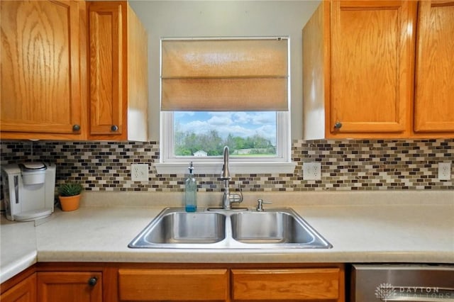 kitchen with stainless steel dishwasher, a sink, backsplash, and light countertops