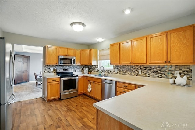 kitchen with a sink, light countertops, light wood-style flooring, stainless steel appliances, and decorative backsplash