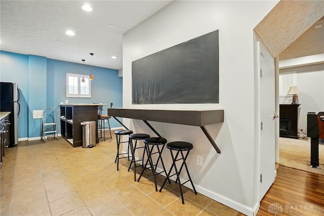 kitchen with light countertops, a breakfast bar area, freestanding refrigerator, recessed lighting, and baseboards