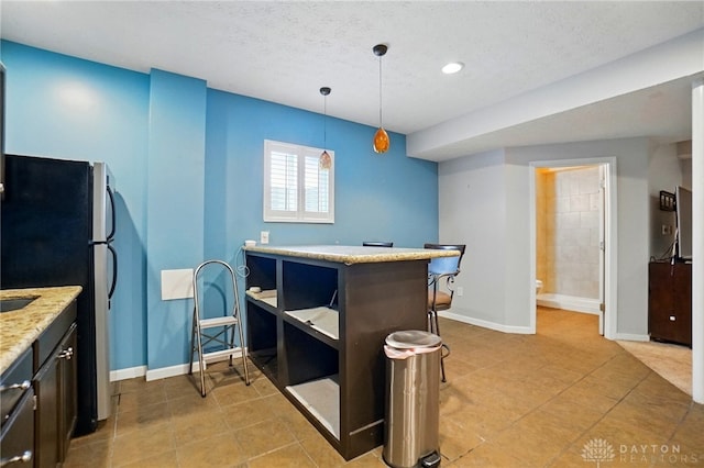 kitchen featuring light tile patterned floors, baseboards, freestanding refrigerator, and decorative light fixtures