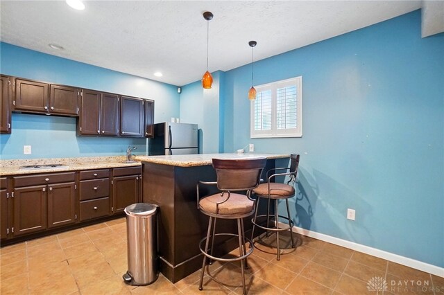 kitchen with a breakfast bar area, dark brown cabinetry, decorative light fixtures, and stainless steel appliances