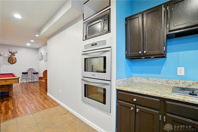kitchen featuring dark brown cabinets, light stone countertops, stainless steel appliances, recessed lighting, and baseboards