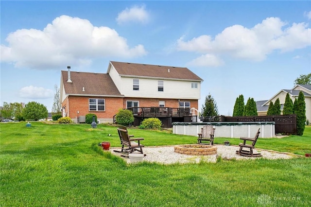 back of property with a wooden deck, a yard, an outdoor fire pit, and brick siding