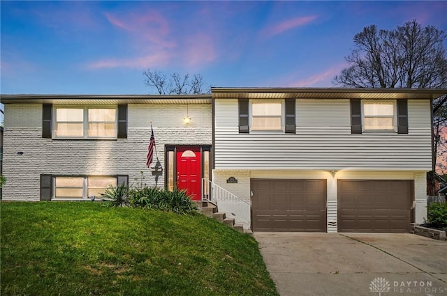 split foyer home with a garage, a lawn, concrete driveway, and brick siding