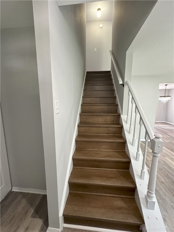 stairway with baseboards, an inviting chandelier, and wood finished floors