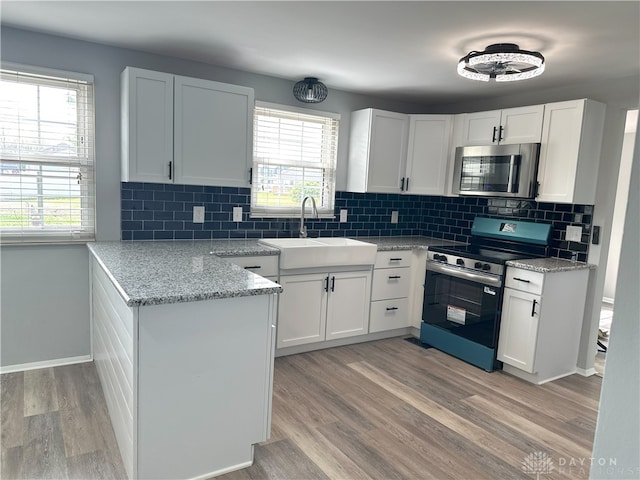 kitchen with a peninsula, appliances with stainless steel finishes, white cabinetry, and a sink