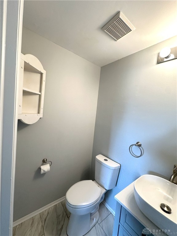 half bathroom featuring vanity, toilet, marble finish floor, baseboards, and visible vents