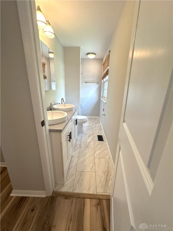 full bath featuring a sink, double vanity, toilet, marble finish floor, and baseboards