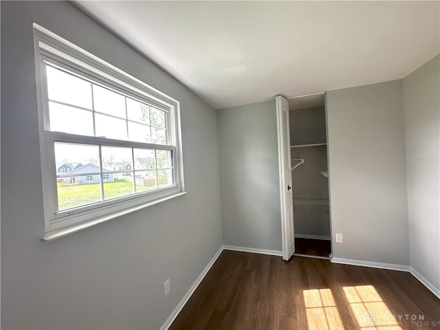 unfurnished bedroom with dark wood-style flooring, baseboards, and a closet