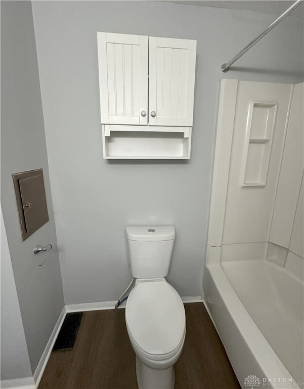 bathroom with baseboards, shower / bathtub combination, toilet, and wood finished floors