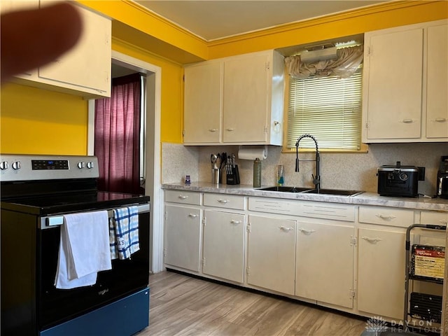 kitchen featuring electric range, a sink, light wood-style floors, light countertops, and decorative backsplash