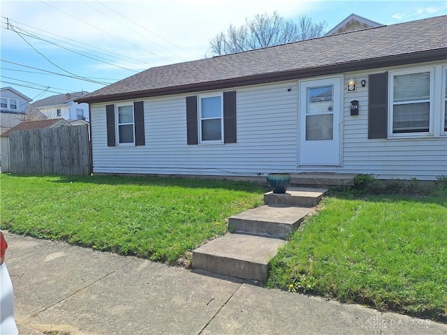 ranch-style home featuring a front lawn, roof with shingles, and fence