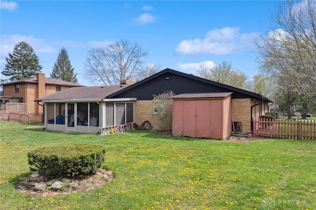 back of house with fence, a storage unit, brick siding, a sunroom, and a lawn