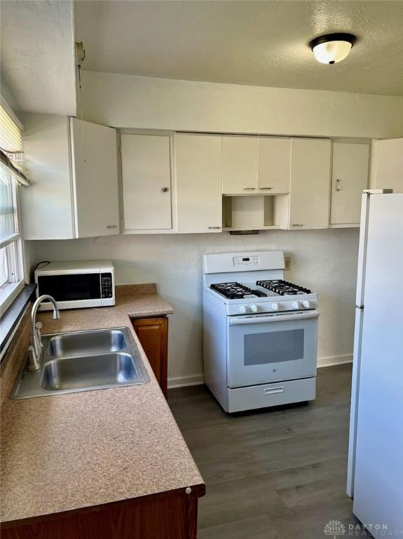 kitchen featuring a sink, baseboards, white cabinets, white appliances, and dark wood-type flooring
