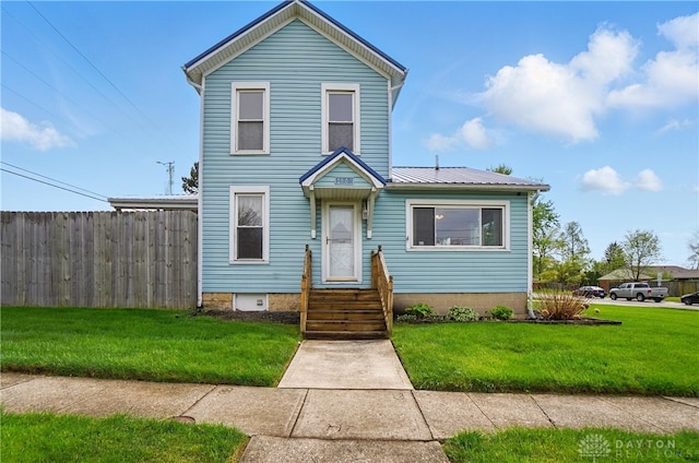 traditional home featuring fence, a front yard, and metal roof