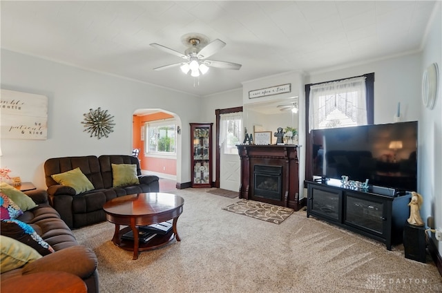 carpeted living area with crown molding, arched walkways, ceiling fan, and a wealth of natural light