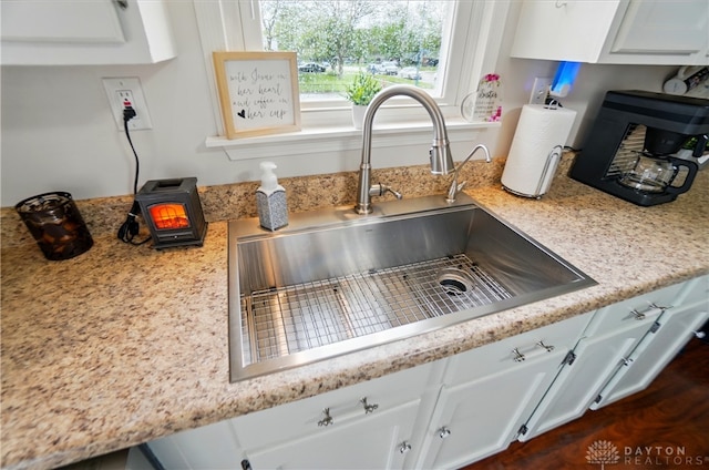 room details with a sink, white cabinets, and a wood stove