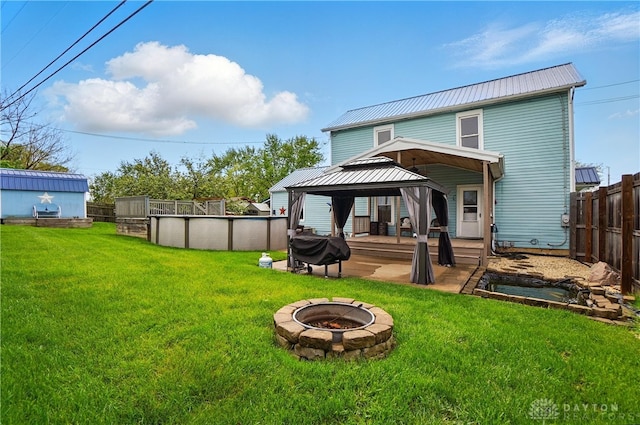 rear view of property with a fenced backyard, an outdoor pool, metal roof, a gazebo, and an outdoor fire pit