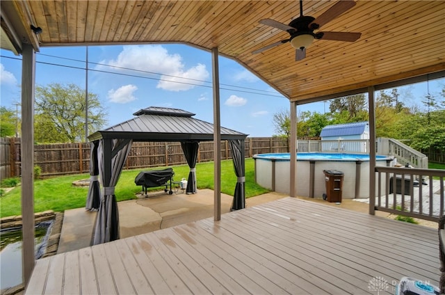 deck with a gazebo, ceiling fan, a fenced backyard, a fenced in pool, and a lawn