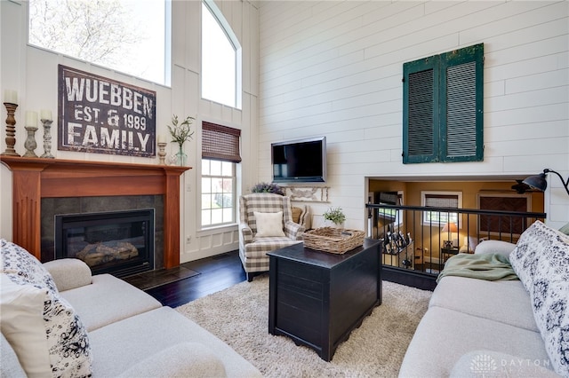 living room with wood walls, a glass covered fireplace, wood finished floors, a towering ceiling, and visible vents