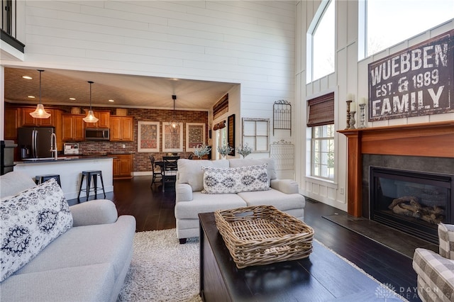 living room featuring wood walls, a glass covered fireplace, a towering ceiling, dark wood-type flooring, and recessed lighting