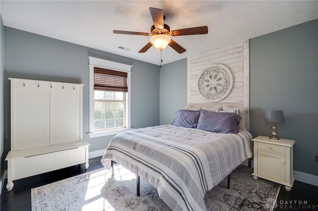 bedroom featuring visible vents, a ceiling fan, baseboards, and dark wood-type flooring