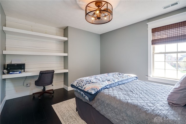bedroom featuring built in study area, dark wood finished floors, baseboards, and visible vents