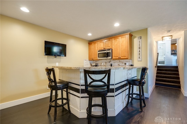 kitchen featuring baseboards, dark wood finished floors, stainless steel microwave, and a kitchen breakfast bar