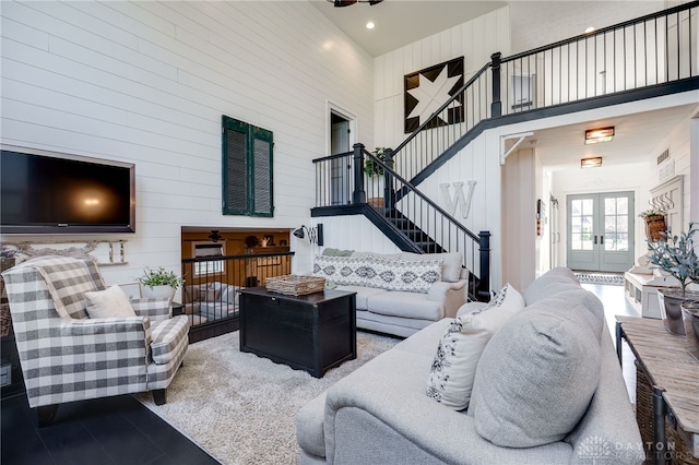 living area featuring stairway, a high ceiling, french doors, and wooden walls