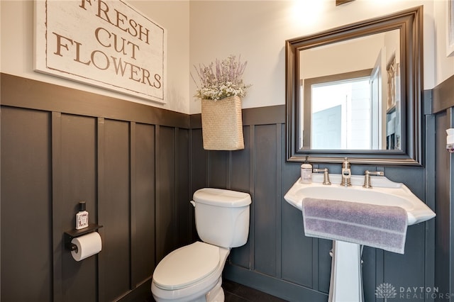 bathroom featuring a decorative wall, a wainscoted wall, and toilet
