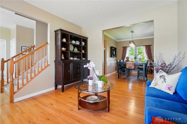 living room with crown molding, baseboards, stairs, and light wood-style floors