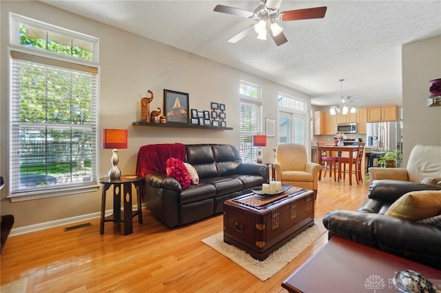 living area with baseboards, visible vents, ceiling fan with notable chandelier, and light wood-type flooring